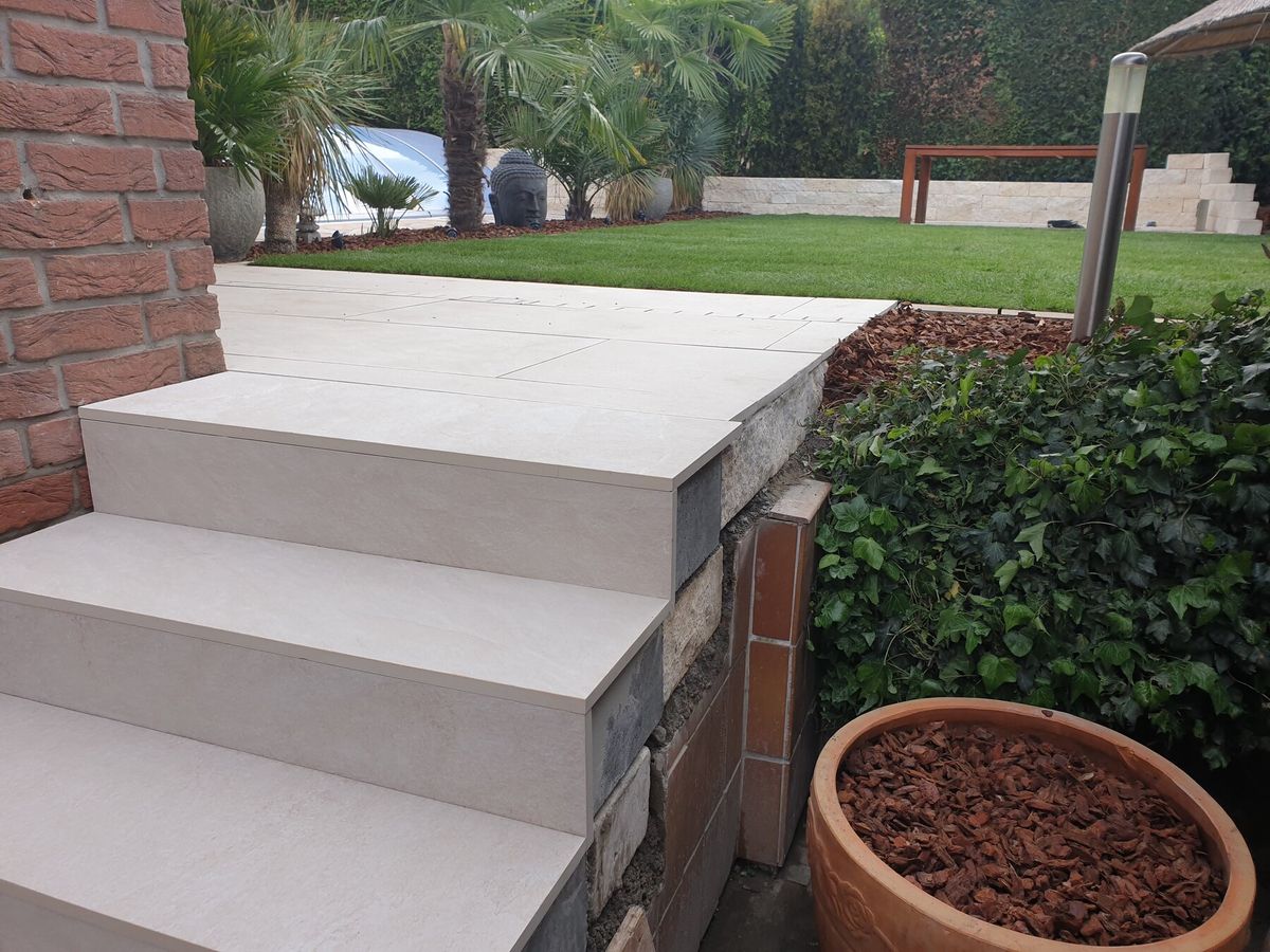 Terrassentreppe mit Naturstein-Sockel, im Hintergrund Rasen und Mauer