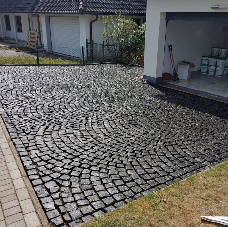 Hofeinfahrt aus Granit-Kleinpflaster im Segmentbogen vor einer offenen Garage