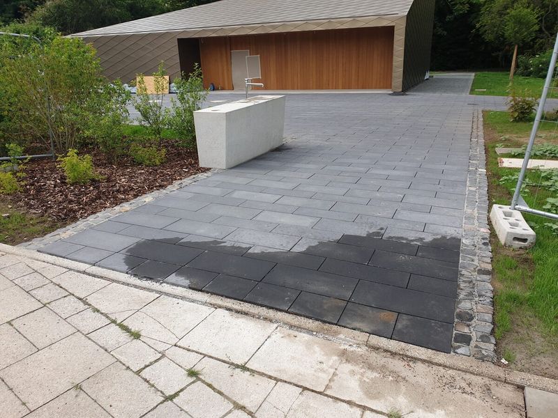 Anthrazitfarbenes Plattenpflaster mit Kleinsteinbord, daneben Beet mit Rindenmulch